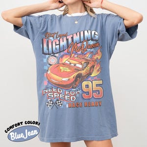 Puede incluir: Camiseta azul vaquero con un gr&aacute;fico de Rayo McQueen de la pel&iacute;cula Cars. El dise&ntilde;o incluye el texto "Street Legend Lightning McQueen", "Need for Speed" y "Race Ready". La camiseta tiene cuello blanco y mangas cortas.