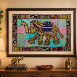 Könnte beinhalten: Gerahmtes Textilkunstwerk mit einem verzierten Elefanten. Der Elefant ist goldfarben mit detaillierten Mustern, vor einem Patchwork-Hintergrund aus Rosa, Blau und Grün. Der dunkelbraune Rahmen umgibt das Kunstwerk, das auf einer Holzoberfläche ausgestellt ist.