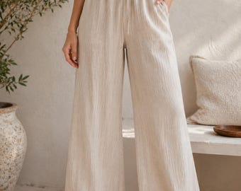 May include: High-waisted, wide-leg trousers in a light beige color with a textured fabric finish. These pants feature an elastic waistband with a matching drawstring tie and two side pockets, paired with a simple white ribbed crop top.