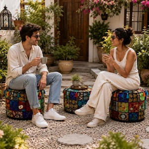 May include: A couple are seated outdoors, each holding a mug. They are sitting on colourful, patchwork-style ottomans. The scene is surrounded by lush greenery and potted plants, creating a relaxed, garden-like atmosphere.