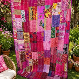 May include: A colourful patchwork quilt in shades of pink and magenta, displayed outdoors. The quilt features a variety of patterned fabrics, including floral and geometric designs. The edges are finished with a solid magenta border, creating a striking visual contrast.