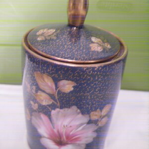 May include: A blue and gold ceramic jar with a floral design. The jar has a lid with a gold knob.