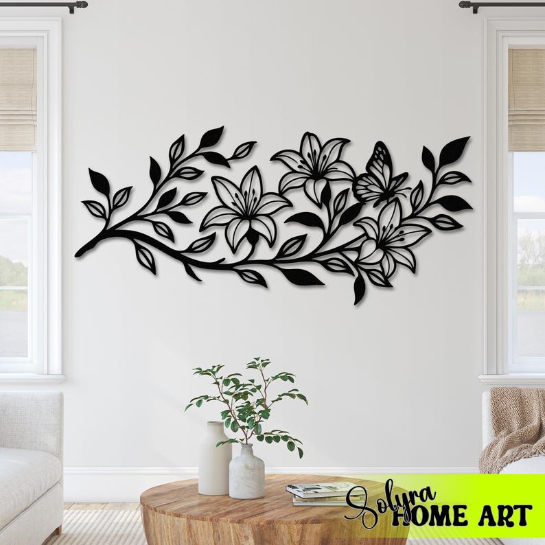 Puede incluir: Arte mural de metal negro que representa una rama floral con lirios y una mariposa. El dise&ntilde;o presenta recortes detallados de hojas y p&eacute;talos de flores, creando un acento decorativo para espacios interiores. El arte est&aacute; montado en una pared blanca.
