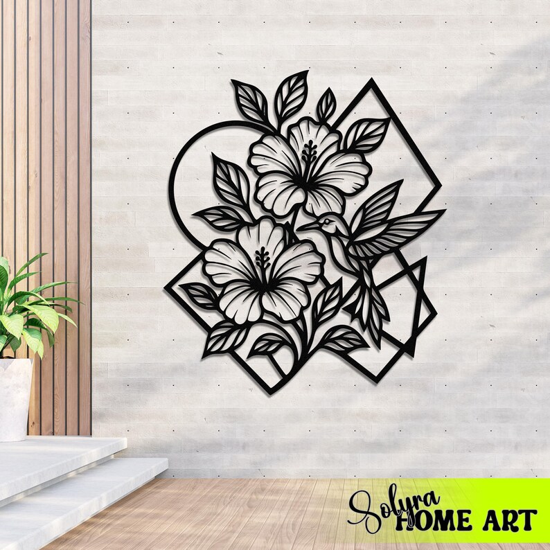 May include: Black metal wall art featuring hibiscus flowers, leaves, a hummingbird, and geometric shapes. The artwork is mounted on a light gray textured wall. The bottom right corner has the text "Solyra HOME ART".
