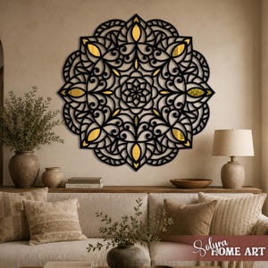 May include: A circular wall art piece featuring an intricate black laser-cut mandala pattern with gold-colored accents visible through the cutouts. The design consists of symmetrical floral and geometric shapes arranged in a radial pattern.