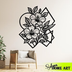 May include: Black metal wall art featuring hibiscus flowers and a hummingbird within geometric shapes. The design includes a circle, square, and triangle. The text "Solyra HOME ART" is visible in the bottom right corner.