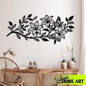 Puede incluir: Arte mural de metal negro que representa una rama floral con lirios y una mariposa. El dise&ntilde;o incluye hojas y p&eacute;talos de flores detallados, creando una pieza decorativa inspirada en la naturaleza.
