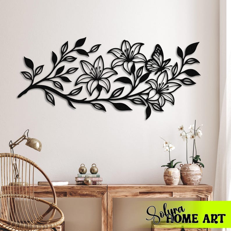Puede incluir: Arte mural de metal negro que representa una rama floral con lirios y una mariposa. El dise&ntilde;o incluye hojas y p&eacute;talos de flores detallados, creando una pieza decorativa inspirada en la naturaleza.