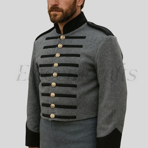 May include: A gray military-style jacket with black trim and gold-colored buttons. The jacket features a high collar and horizontal black stripes across the chest. The sleeves have black cuffs. The jacket is made of a wool-like material.
