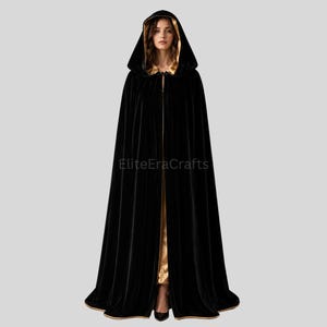 May include: A floor-length black velvet cloak featuring a deep hood and a contrasting metallic gold lining. The garment is fastened at the neck and displays the text EliteEraCrafts across the center. The fabric drapes fully to the floor.