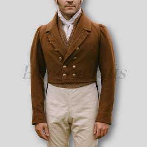 Op de afbeelding: Een bruine dubbelbreasted jas met gouden knopen. De jas heeft een getailleerde pasvorm en wordt gedragen met een wit overhemd en een crème broek. De mouwen zijn licht gezwollen bij de schouders.