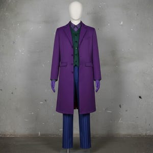 May include: A purple long coat worn over a dark green button-up vest, a purple patterned dress shirt, and blue pinstriped trousers. The ensemble includes a pair of purple gloves, displayed on a mannequin against a plain gray wall.