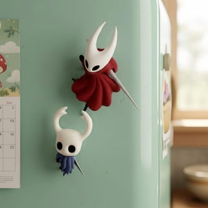 May include: Two character-shaped magnets. One is white with a red cape and a silver sword. The other is white with a blue cape and a silver sword. Both are attached to a light green fridge.