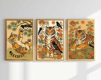 May include: Set of three framed art prints featuring stylized tigers and birds. The tigers are depicted in orange and black stripes, with black birds perched nearby. The backgrounds include floral and foliage elements in shades of orange, green, and beige.