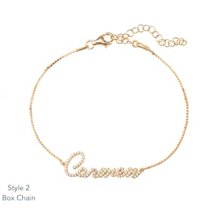 Puede incluir: Una pulsera de cadena tipo caja dorada con el nombre "Carmen" escrito en cursiva, adornada con peque&ntilde;as piedras brillantes. La pulsera tiene una longitud ajustable y un cierre de mosquet&oacute;n. El texto "Style 2 Box Chain" est&aacute; en la esquina inferior izquierda.