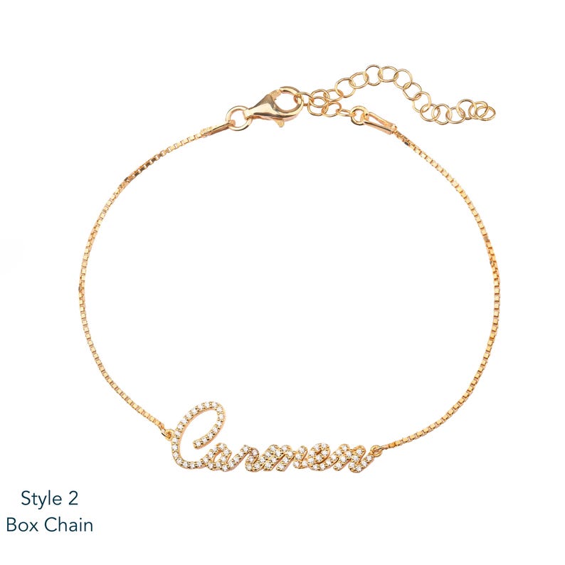 Puede incluir: Una pulsera de cadena tipo caja dorada con el nombre "Carmen" escrito en cursiva, adornada con peque&ntilde;as piedras brillantes. La pulsera tiene una longitud ajustable y un cierre de mosquet&oacute;n. El texto "Style 2 Box Chain" est&aacute; en la esquina inferior izquierda.