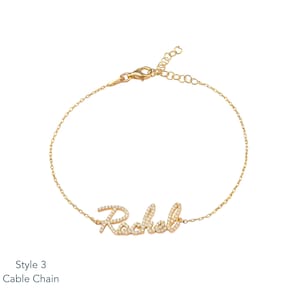 Puede incluir: Una pulsera de cadena dorada con el nombre "Rachel" escrito en cursiva, incrustado con peque&ntilde;as piedras preciosas transparentes. La pulsera tiene un cierre de mosquet&oacute;n y una cadena ajustable. El texto "Style 3 Cable Chain" est&aacute; en la esquina inferior izquierda.