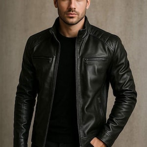 Puede incluir: Chaqueta de cuero negra con cuello alzado y detalles acolchados en los hombros. La chaqueta tiene dos bolsillos con cremallera en el pecho y cierre de cremallera frontal. El modelo viste camisa y pantalón negros.