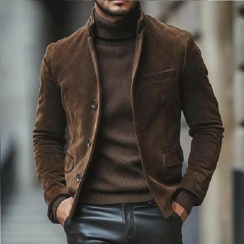 May include: A brown suede jacket with a three-button closure, paired with a brown turtleneck sweater. The jacket has two front pockets and a classic collar. The outfit is completed with black leather pants.