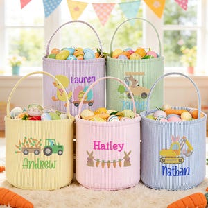 Op de afbeelding: Vijf paasmanden in pastelkleuren, gevuld met decoratieve eieren. Elke mand heeft een handvat en is gepersonaliseerd met een naam en een thema-afbeelding, zoals een tractor of een konijn. De manden staan op een wit tapijt met worteldecoraties.