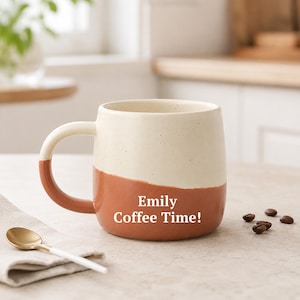 Op de afbeelding: Een tweekleurige keramische mok met een crèmekleurige bovenkant en een terracotta onderkant. De mok is voorzien van de witte tekst "Emily Coffee Time!" op de voorzijde. Het heeft een gebogen handvat en een gespikkelde textuur.