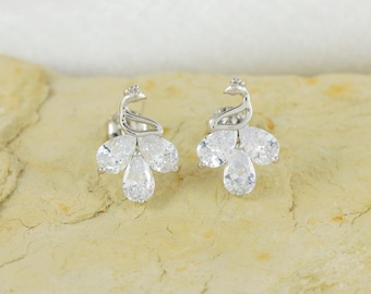 May include: A pair of silver-toned stud earrings shaped like stylized birds, each featuring three clear, pear-shaped faceted stones arranged to form the body and tail, with a curved metal neck and head design.