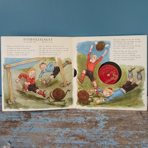 Könnte beinhalten: Ein aufgeschlagenes Kinderbuch mit dem Titel FOTBOLLSLAGET mit farbenfrohen Illustrationen von Kindern, die in roten und blauen Trikots Fußball spielen. Ein kreisförmiger Ausschnitt auf der rechten Seite zeigt eine rote Schallplatte mit dem Text Pagoton.