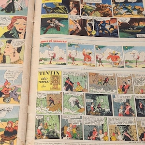 Puede incluir: Una revista de c&oacute;mic vintage abierta que presenta m&uacute;ltiples paneles y tiras ilustradas a color. Las p&aacute;ginas contienen varios personajes y globos de di&aacute;logo en diferentes idiomas, con el t&iacute;tulo Tintin claramente visible en una de las secciones.