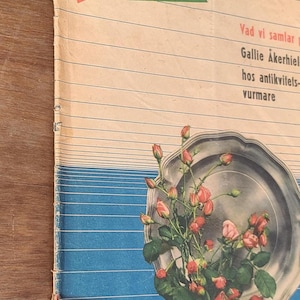 Puede incluir: Una revista vintage titulada Familie Journalen con un gr&aacute;fico de una bandeja de plata llena de capullos de rosa rosados y hojas verdes. La portada tiene l&iacute;neas horizontales, una secci&oacute;n inferior azul y texto como Vad vi samlar.