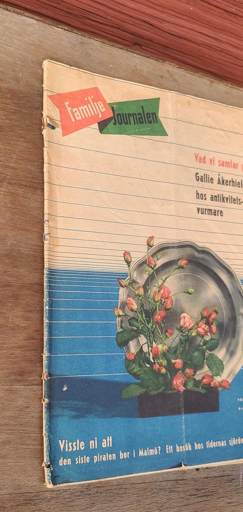 Puede incluir: Una revista vintage titulada Familie Journalen con un gr&aacute;fico de una bandeja de plata llena de capullos de rosa rosados y hojas verdes. La portada tiene l&iacute;neas horizontales, una secci&oacute;n inferior azul y texto como Vad vi samlar.
