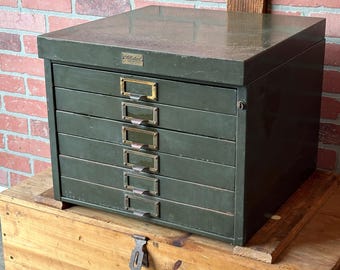 May include: A vintage green metal filing cabinet with six drawers and brass pulls. The cabinet has a label on the top that reads "Old Metal".