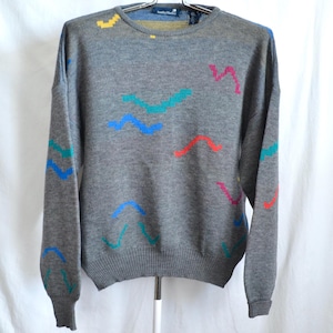 May include: A gray sweater with a colorful abstract pattern. The sweater has long sleeves and a crew neck. The pattern is made up of wavy lines in shades of blue, green, red, and yellow.