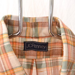 May include: A plaid shirt with a brown, orange, and green plaid pattern. The shirt has a label that says "JCPenney".