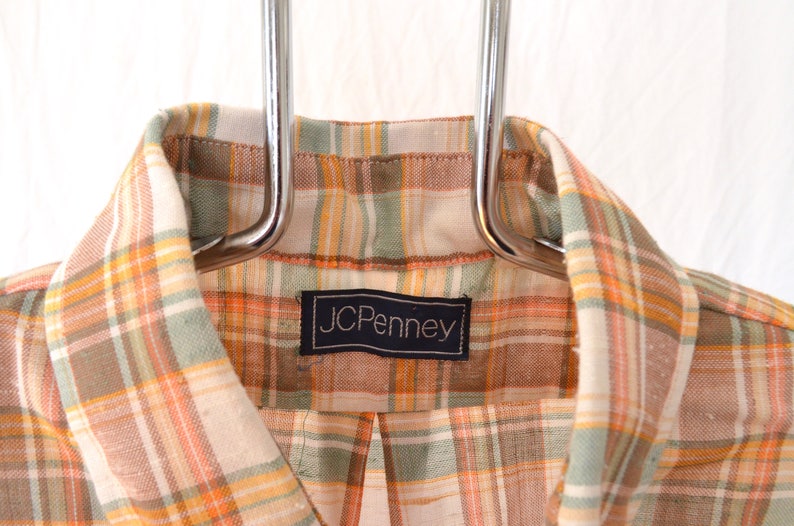 May include: A plaid shirt with a brown, orange, and green plaid pattern. The shirt has a label that says "JCPenney".
