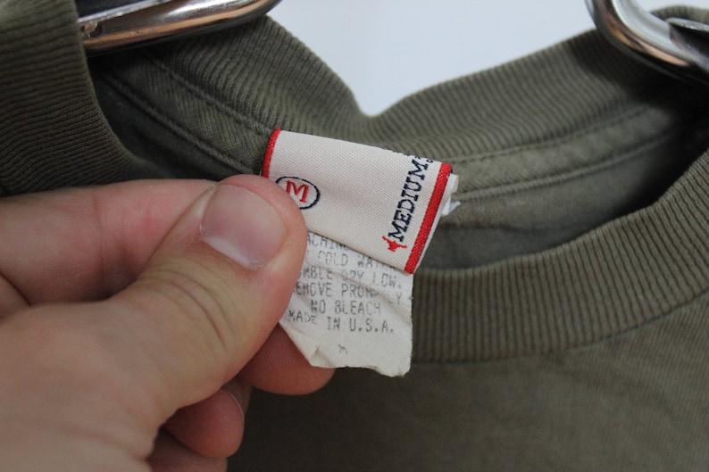 Op de afbeelding: Een groen T-shirt met een wit label waarop "Medium" staat en wasinstructies. Het label vermeldt ook "Made in U.S.A."