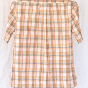 May include: A short-sleeved button-down shirt with a plaid pattern in shades of orange, brown, and white.