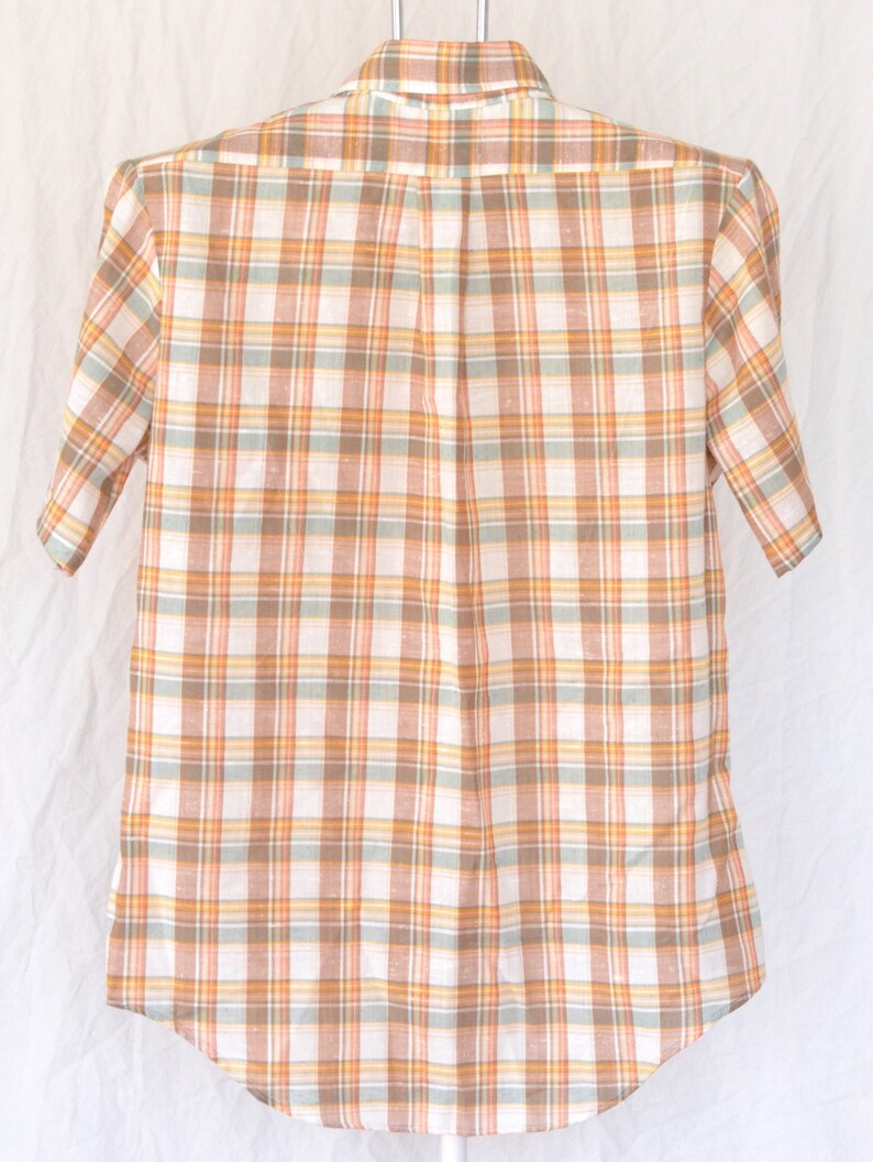 May include: A short-sleeved button-down shirt with a plaid pattern in shades of orange, brown, and white.