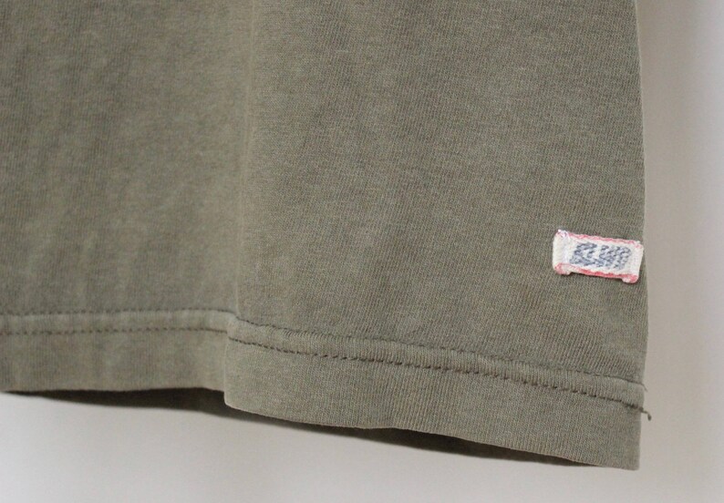Op de afbeelding: Een close-up van de zoom van een groen T-shirt met een klein wit label met de tekst "R.L.P.D."