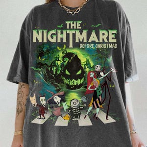 K&ouml;nnte beinhalten: Dunkelgraues T-Shirt mit einer Grafik aus "The Nightmare Before Christmas". Das Design zeigt Charaktere, die einen Zebrastreifen &uuml;berqueren, mit einem gruseligen Hintergrund und dem Text "The Nightmare Before Christmas."