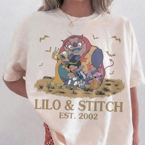 K&ouml;nnte beinhalten: Cremefarbenes T-Shirt mit einem Halloween-Motiv von Lilo & Stitch. Unter der Illustration steht der Text "LILO & STITCH EST. 2002". Das Shirt ist von der Marke Comfort Colors.