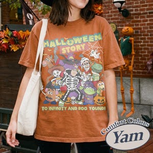 May include: Orange Comfort Colors t-shirt with a Halloween-themed graphic. The graphic features cartoon characters, a spiderweb, and the text "HALLOWEEN STORY" and "TO INFINITY AND BOO YOUND!"