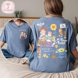 Puede incluir: Camiseta azul con un dise&ntilde;o de Toy Story. La parte delantera muestra una peque&ntilde;a imagen con el texto "you've got a friend in me". La parte trasera presenta un dise&ntilde;o m&aacute;s grande con "Pizza Planet" y personajes de Toy Story.