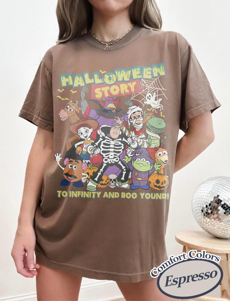 May include: Brown t-shirt with a Halloween-themed graphic featuring cartoon characters and the text "HALLOWEEN STORY" and "TO INFINITY AND BOO YOND!". The shirt is a Comfort Colors Espresso.