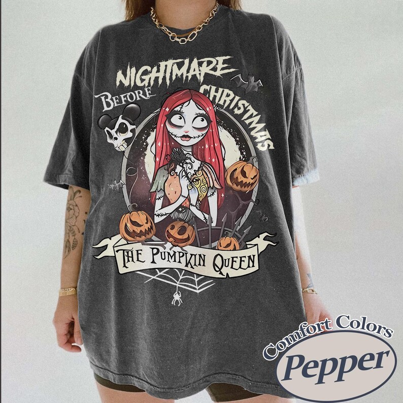 Puede incluir: Camiseta gris oscuro con un dise&ntilde;o gr&aacute;fico de "Pesadilla antes de Navidad". El dise&ntilde;o incluye a Sally, calabazas y el texto "The Pumpkin Queen". La camiseta tiene un aspecto vintage y la etiqueta Comfort Colors Pepper.