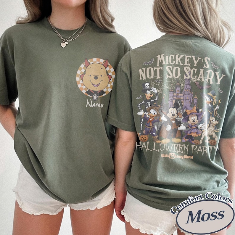 May include: Olive green t-shirts with Halloween-themed graphics. One shirt features Winnie the Pooh in a costume with the word "Name" below. The other shirt displays "Mickey's Not So Scary Halloween Party" with Disney characters and a castle.