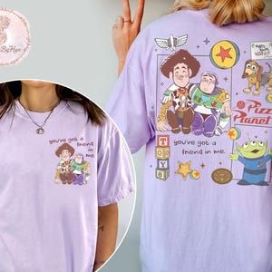 Puede incluir: Camiseta lila con un dise&ntilde;o de Toy Story. La parte delantera muestra a Woody y Buzz Lightyear con el texto "you've got a friend in me". La parte trasera presenta m&aacute;s personajes y el logo de Pizza Planet.