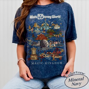 Puede incluir: Camiseta azul marino con un gr&aacute;fico colorido de atracciones y personajes de Walt Disney World. La camiseta incluye el texto "Walt Disney World" y "Magic Kingdom". La camiseta tiene un efecto de lavado mineral y es de material suave.