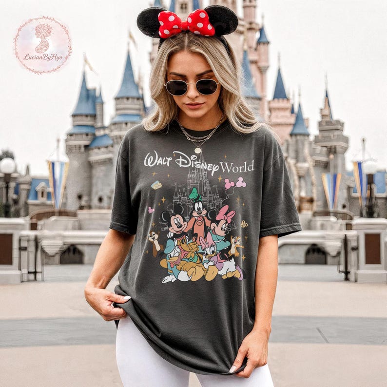 May include: Dark gray t-shirt featuring the text "Walt Disney World" above a graphic of Disney characters, including Mickey Mouse, Minnie Mouse, and Goofy. The shirt has a classic fit and short sleeves.