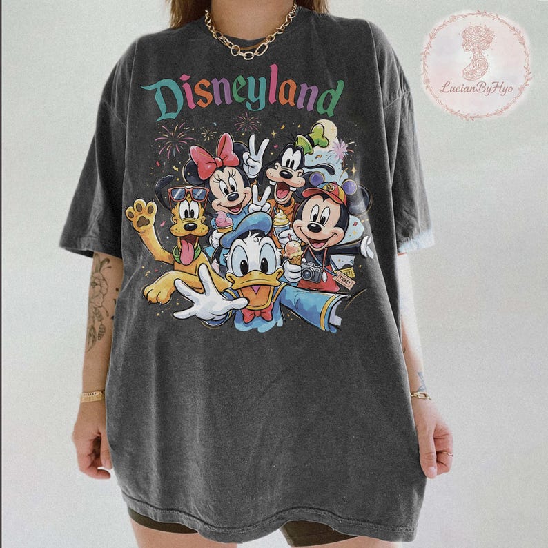 May include: Dark gray t-shirt featuring the word "Disneyland" in colorful text above a graphic of Disney characters including Mickey Mouse, Minnie Mouse, Donald Duck, Goofy, and Pluto. The shirt has a vintage, worn look.