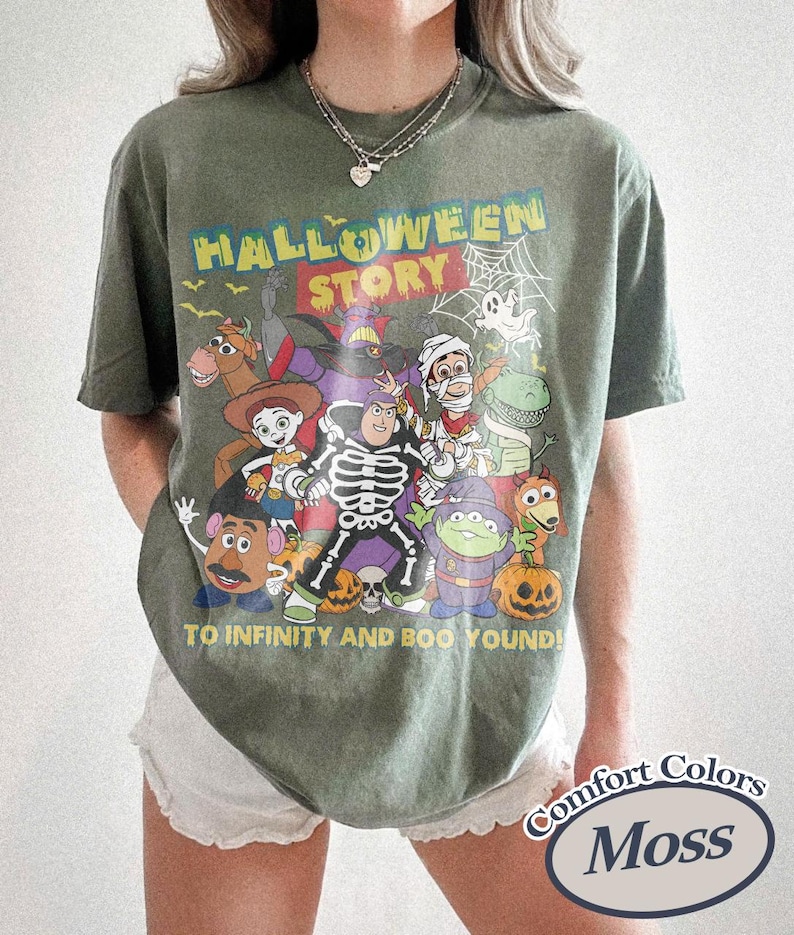 May include: Moss green Comfort Colors t-shirt with a Halloween-themed graphic. The graphic features various cartoon characters, the words "HALLOWEEN STORY", and the phrase "TO INFINITY AND BOO YOUND!"